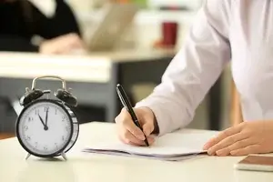 Notizen machende Person / Ein Wecker im Vordergrund